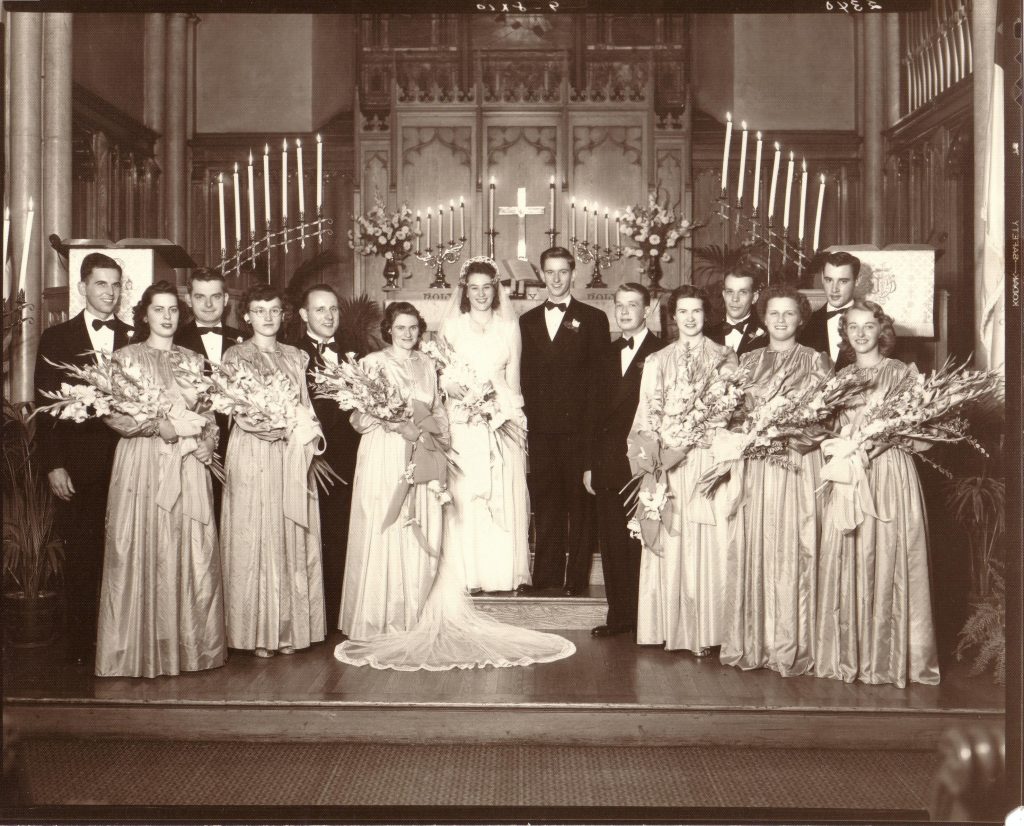 A bridal party stands with the bride and groom on a church altar in 1946